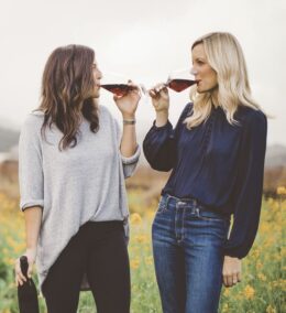 Two female entrepreneurs of ONEHOPE wine sipping red wine from glasses in front of winery celebrating women's history month