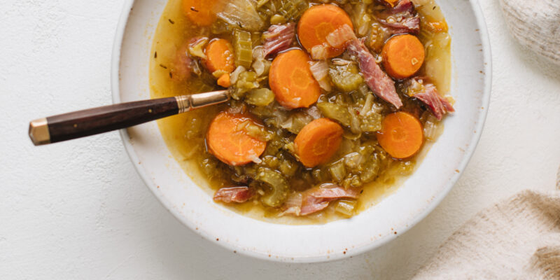 A pot of red curry split pea soup with carrots, celery, and ham, served alongside a bowl, ideal for an exotic winter soup and wine pairing with ONEHOPE Vintner Pinot Noir.